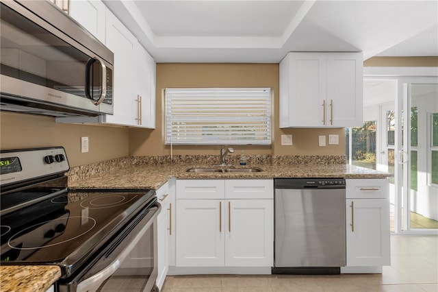 kitchen with sink, white cabinetry, stainless steel appliances, light stone counters, and a tray ceiling