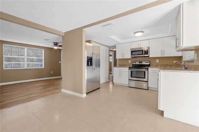 kitchen featuring ceiling fan, white cabinetry, stainless steel appliances, a tray ceiling, and light stone countertops