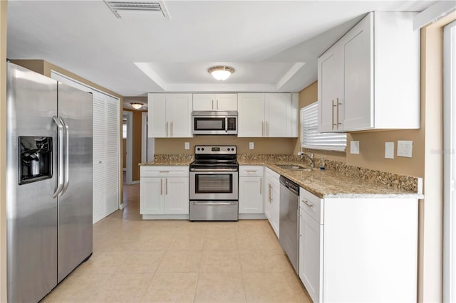 kitchen featuring sink, stainless steel appliances, light stone counters, a tray ceiling, and white cabinets