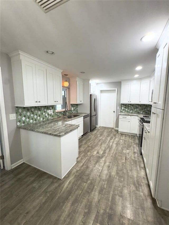 kitchen with appliances with stainless steel finishes, dark hardwood / wood-style floors, white cabinetry, dark stone counters, and kitchen peninsula