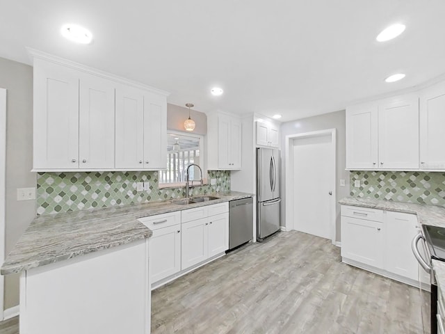 kitchen featuring light wood finished floors, a peninsula, white cabinets, stainless steel appliances, and a sink