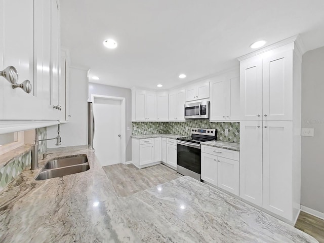 kitchen with light stone counters, decorative backsplash, white cabinets, stainless steel appliances, and a sink