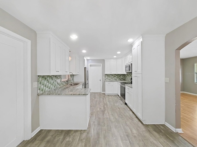 kitchen featuring arched walkways, a sink, stainless steel appliances, white cabinetry, and light wood-type flooring