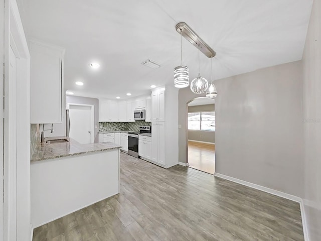 kitchen featuring arched walkways, a sink, decorative backsplash, appliances with stainless steel finishes, and light wood-type flooring