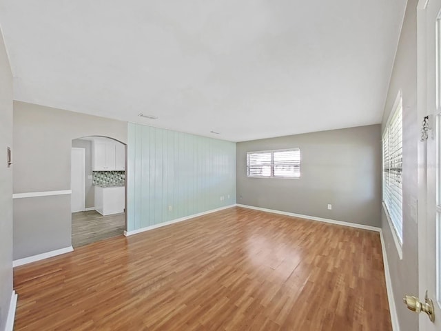 empty room with light wood-type flooring, arched walkways, and baseboards