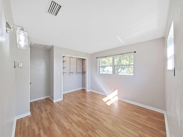 unfurnished bedroom featuring visible vents, baseboards, attic access, light wood-type flooring, and a closet