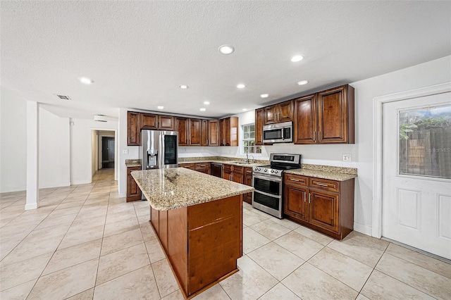 kitchen with light tile patterned floors, light stone counters, a kitchen island, visible vents, and appliances with stainless steel finishes