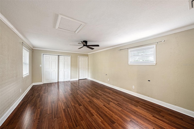 unfurnished bedroom with wood finished floors, ornamental molding, multiple windows, two closets, and attic access