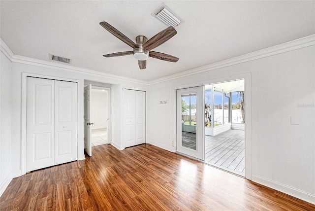 unfurnished bedroom with access to exterior, visible vents, two closets, and wood finished floors