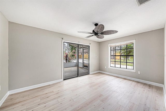 empty room with a ceiling fan, baseboards, a textured ceiling, and light wood finished floors