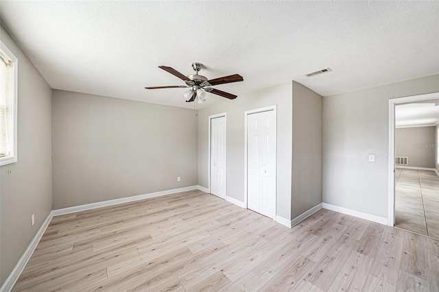 unfurnished bedroom featuring baseboards, visible vents, light wood finished floors, and two closets