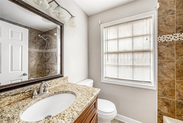 bathroom with baseboards, a tile shower, vanity, and toilet