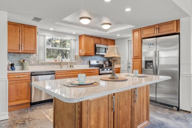 kitchen featuring sink, appliances with stainless steel finishes, a raised ceiling, a kitchen island, and backsplash