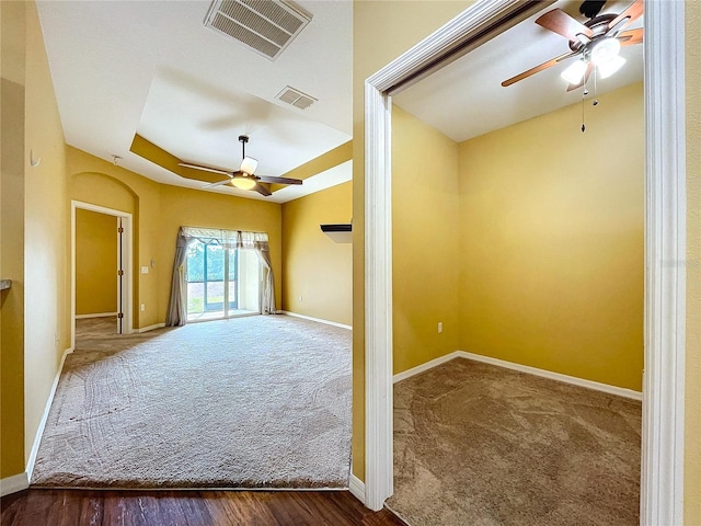 spare room with ceiling fan, a raised ceiling, and dark carpet