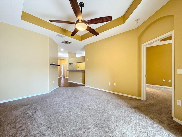 unfurnished living room featuring a raised ceiling, ceiling fan, and dark carpet