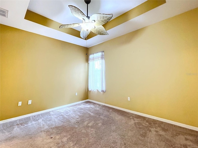 empty room with a raised ceiling, carpet floors, and ceiling fan