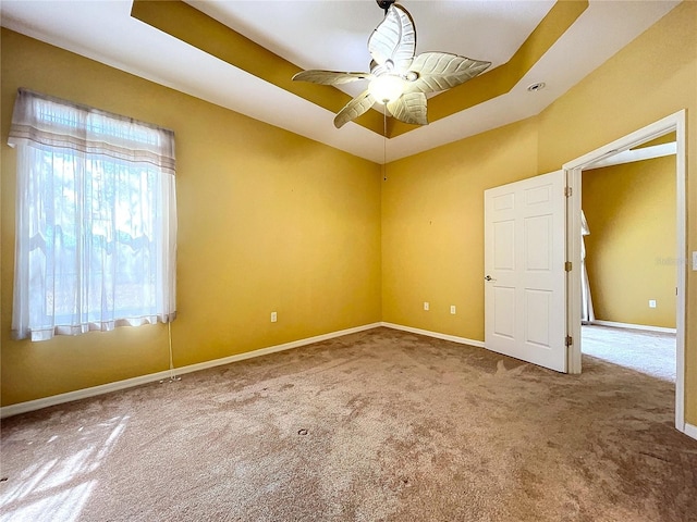 carpeted spare room with a tray ceiling and ceiling fan