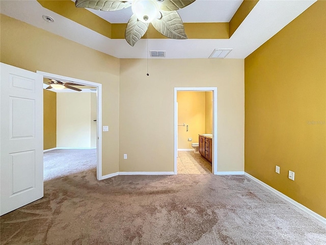 unfurnished bedroom featuring light colored carpet, ensuite bathroom, and a tray ceiling