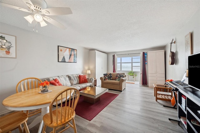 living room with ceiling fan, a textured ceiling, and light hardwood / wood-style flooring