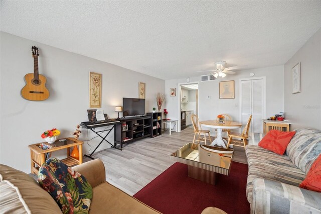 living room featuring ceiling fan, light hardwood / wood-style flooring, and a textured ceiling