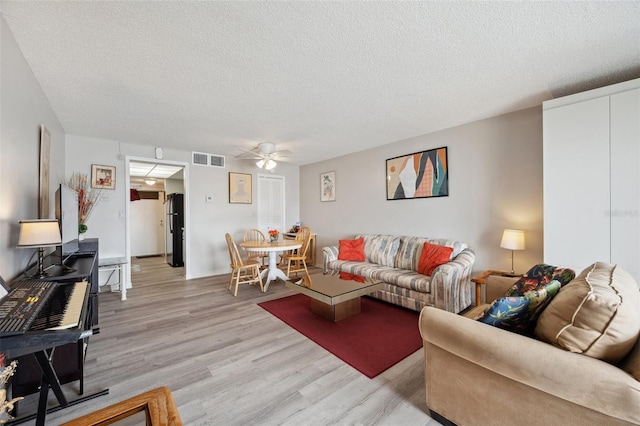 living room with ceiling fan, light hardwood / wood-style flooring, and a textured ceiling