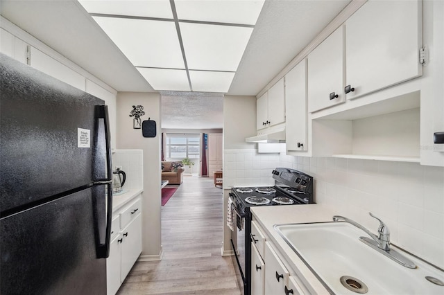 kitchen featuring tasteful backsplash, white cabinetry, sink, black appliances, and light hardwood / wood-style flooring