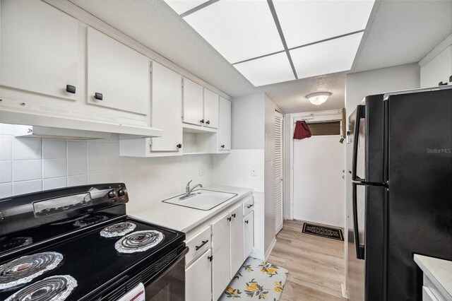 kitchen featuring sink, black appliances, light hardwood / wood-style floors, white cabinets, and decorative backsplash