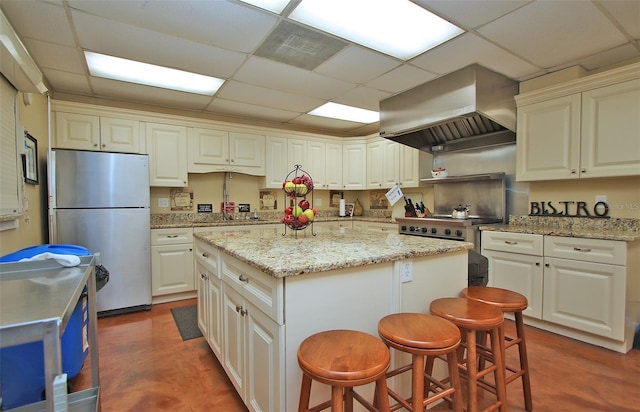 kitchen featuring light stone counters, a paneled ceiling, ventilation hood, appliances with stainless steel finishes, and a kitchen island