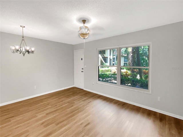 empty room featuring an inviting chandelier, a textured ceiling, baseboards, and wood finished floors