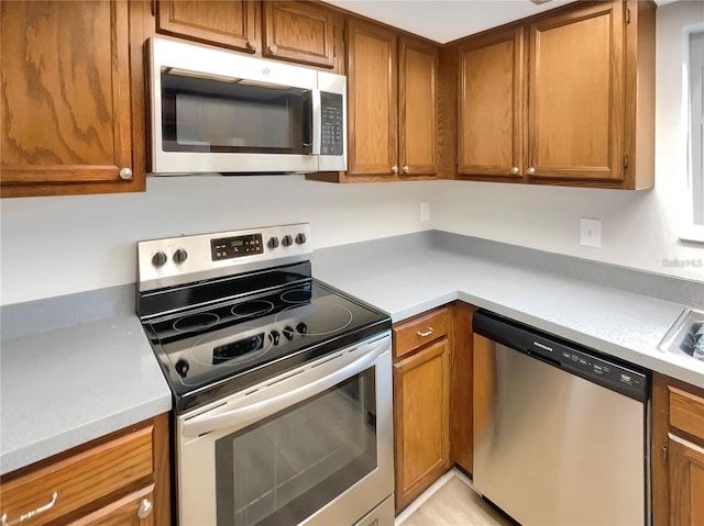 kitchen featuring appliances with stainless steel finishes, brown cabinetry, light countertops, and a sink