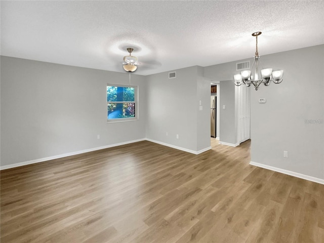 unfurnished room featuring visible vents, a textured ceiling, baseboards, and wood finished floors