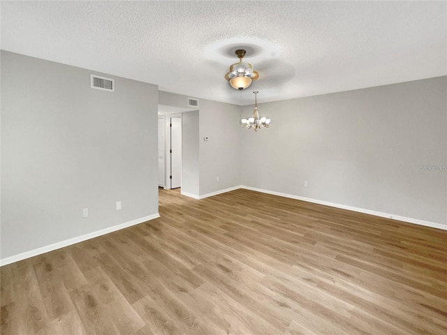 empty room with a textured ceiling, wood finished floors, visible vents, and an inviting chandelier