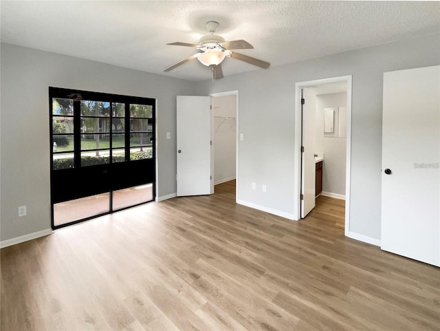 unfurnished bedroom featuring baseboards, access to outside, a spacious closet, a textured ceiling, and light wood-style floors