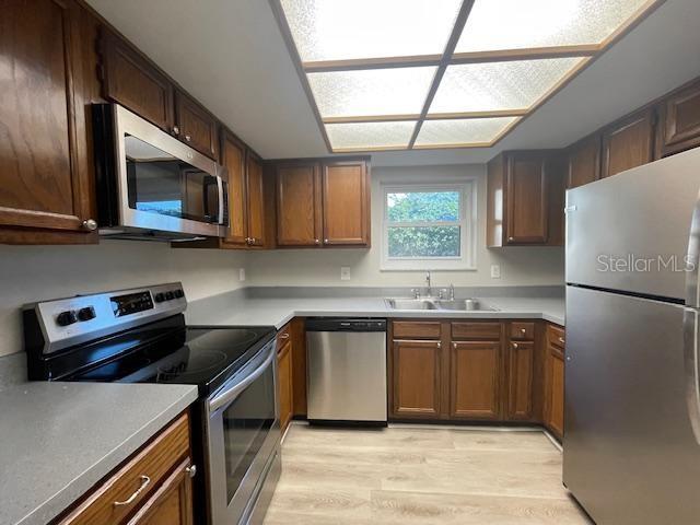 kitchen with stainless steel appliances, light countertops, a sink, and light wood finished floors