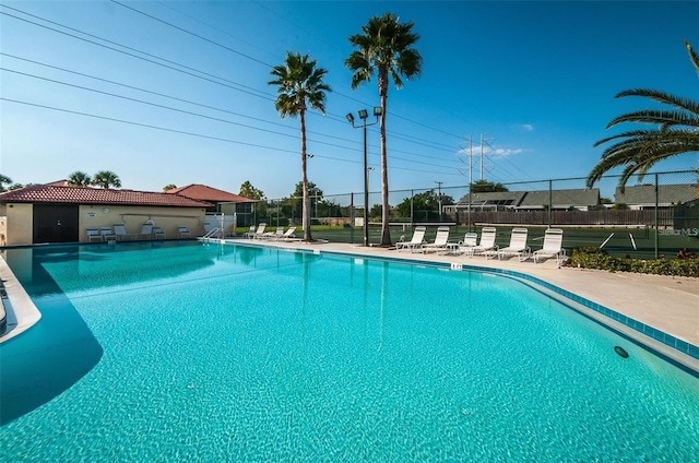 view of swimming pool with a tennis court and fence