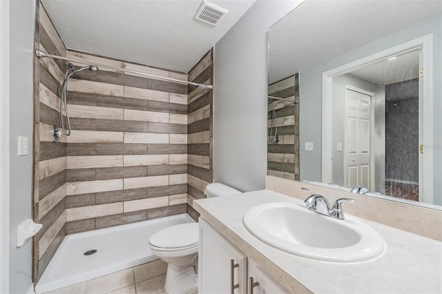 bathroom featuring tile patterned flooring, a tile shower, vanity, a textured ceiling, and toilet