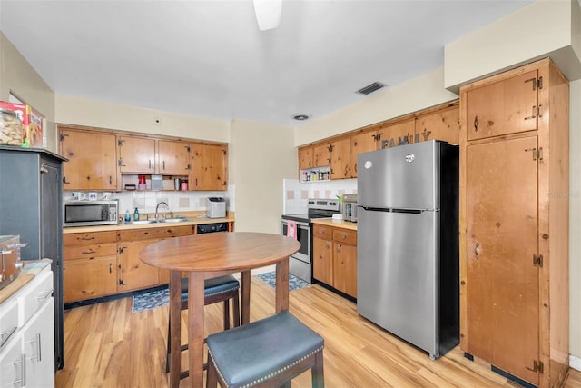 kitchen with stainless steel appliances, sink, light hardwood / wood-style floors, and decorative backsplash