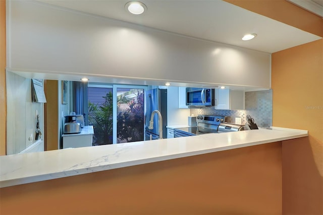 kitchen with tasteful backsplash, white cabinetry, appliances with stainless steel finishes, and kitchen peninsula