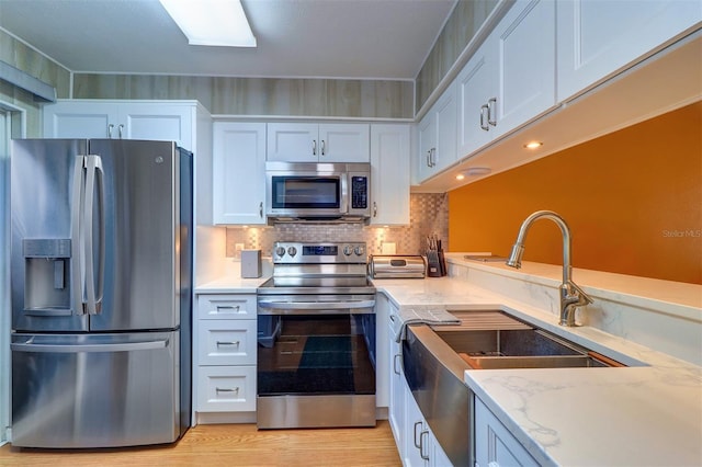 kitchen featuring stainless steel appliances, white cabinetry, sink, and light stone counters