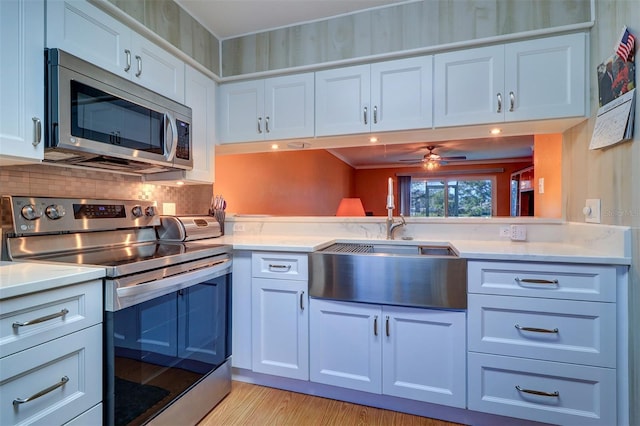 kitchen featuring sink, appliances with stainless steel finishes, white cabinetry, tasteful backsplash, and light hardwood / wood-style floors