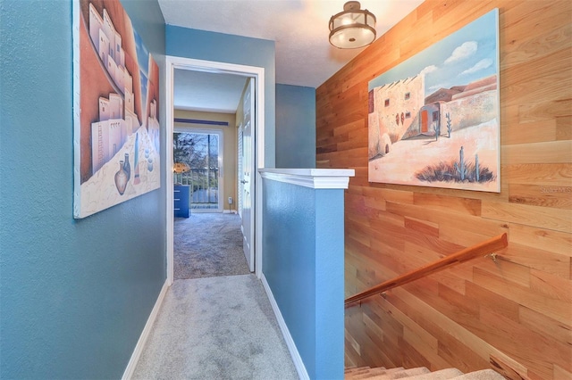 hallway featuring carpet flooring and wood walls