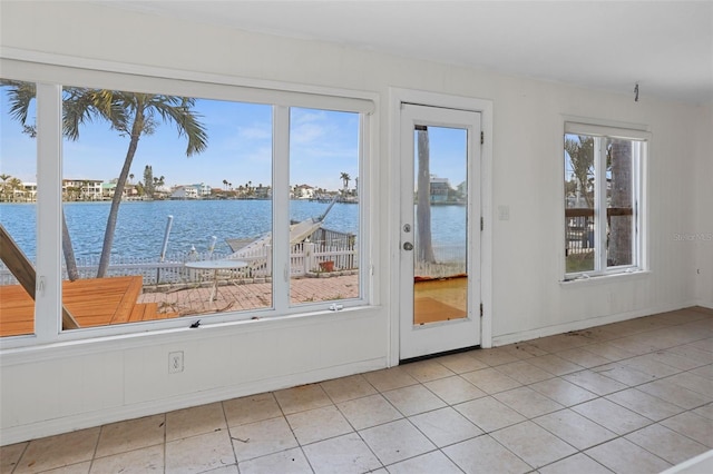 doorway featuring a water view, light tile patterned floors, and baseboards