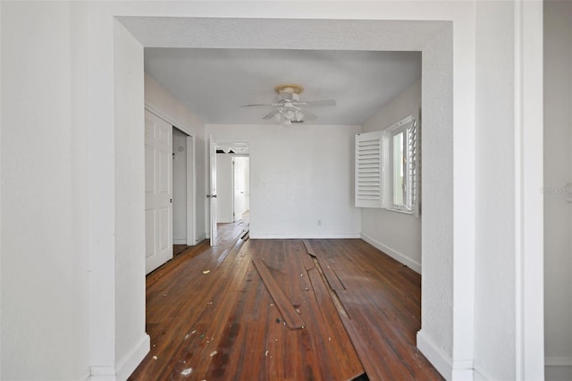 unfurnished room with dark wood-style floors, a ceiling fan, and baseboards