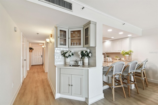 interior space featuring tasteful backsplash, ornamental molding, sink, and light hardwood / wood-style flooring