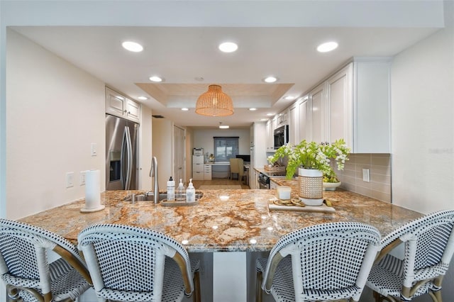 kitchen featuring appliances with stainless steel finishes, sink, white cabinets, kitchen peninsula, and a raised ceiling