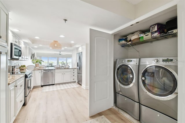 laundry room with sink, washing machine and dryer, and light wood-type flooring