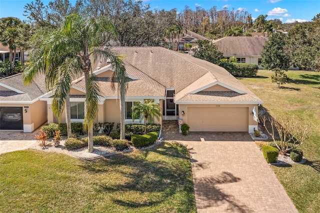 view of front facade featuring a front yard, stucco siding, an attached garage, a shingled roof, and decorative driveway