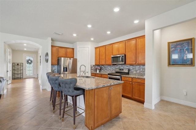 7580 Pool Compass Loop, Wesley Chapel, FL 33545 - kitchen featuring arched walkways, tasteful backsplash, light stone counters, a sink, and appliances with stainless steel finishes