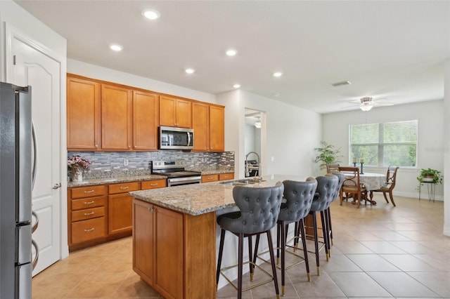7580 Pool Compass Loop, Wesley Chapel, FL 33545 - kitchen with brown cabinetry, backsplash, a sink, stainless steel appliances, and light tile patterned flooring