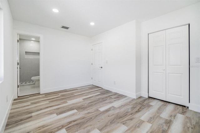 unfurnished bedroom featuring a closet, connected bathroom, and light hardwood / wood-style flooring